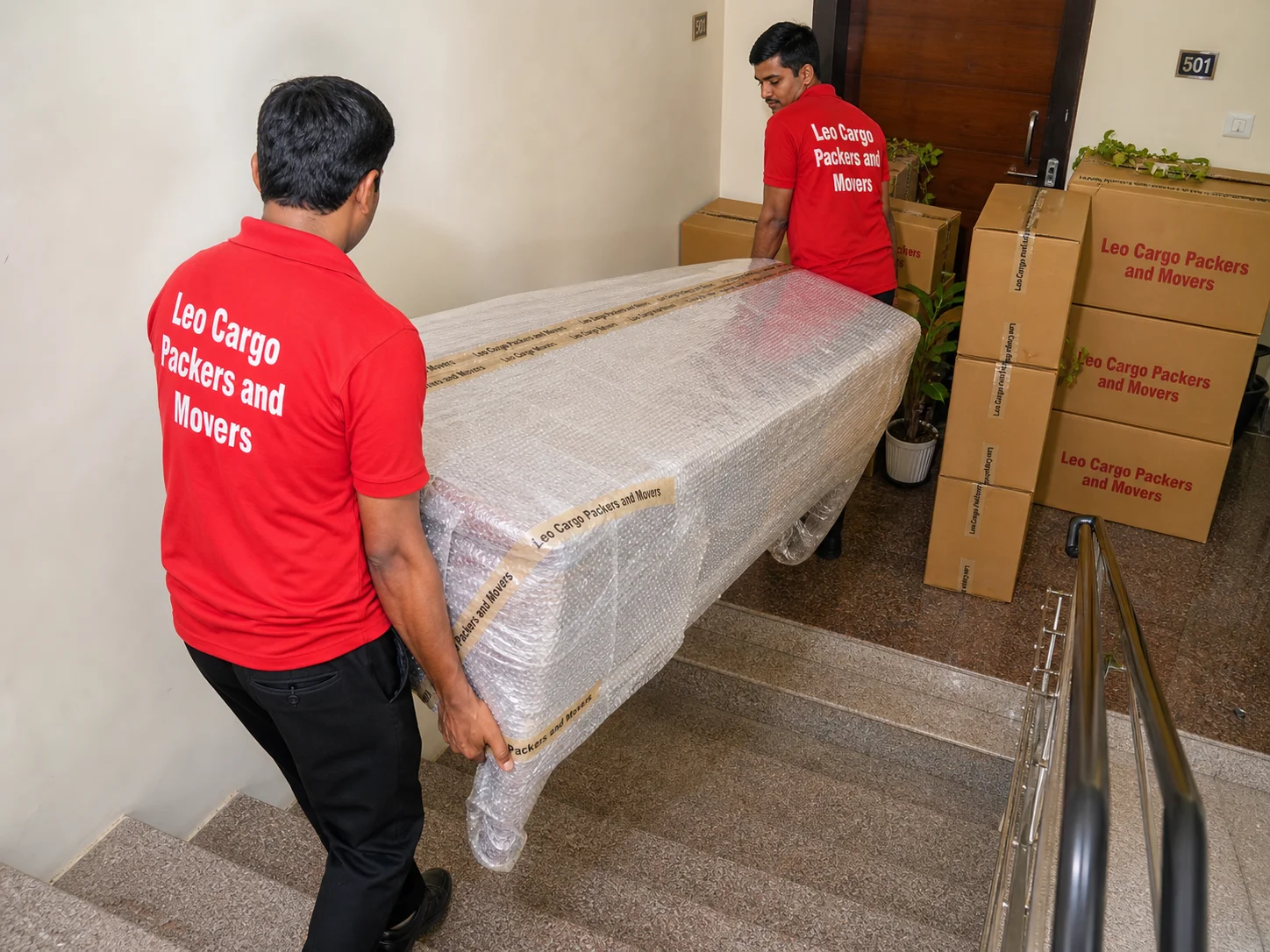 Movers carefully carrying a heavy bubble-wrapped dining table down the stairs of an Indian apartment building - Leo Cargo Packers and Movers